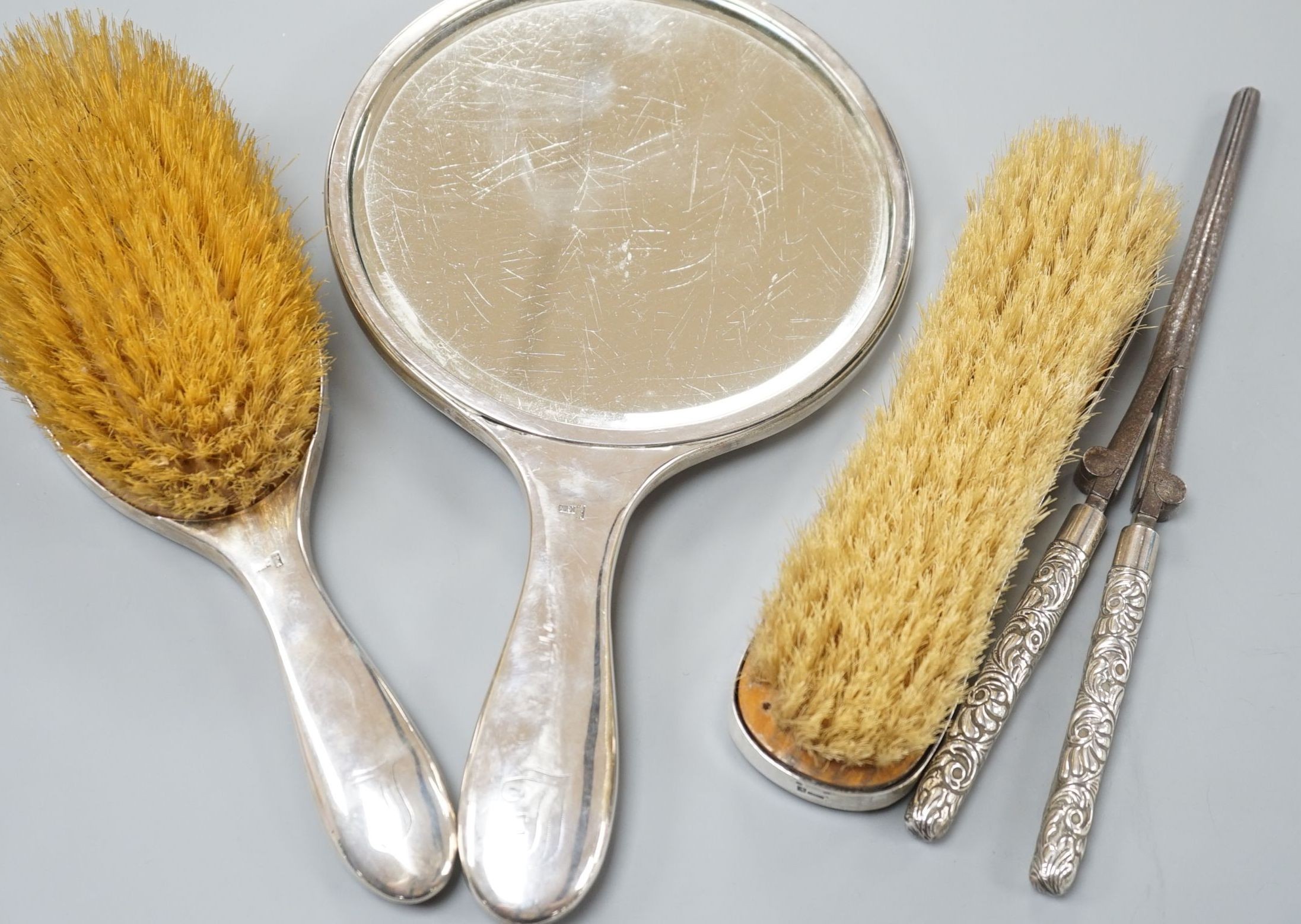 An early 20th century Chinese Export white metal three piece dressing table set, by Wang Hing, Hong Kong, comprising a mirror and two brushes and a pair of associated silver handled curling tongs.